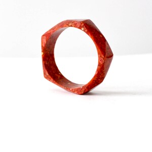 May include: A red, hexagonal-shaped bangle bracelet with a speckled pattern.