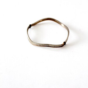 May include: A silver-toned bangle bracelet with a wavy design. The bracelet is made of multiple thin wires that are twisted together.