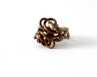 May include: A silver and copper ring with a unique, intricate design. The ring is made of twisted metal and features a series of small, round details.