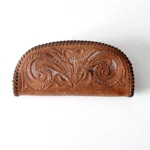 May include: A brown leather wallet with a floral design embossed on the front. The wallet has a stitched edge and is closed.