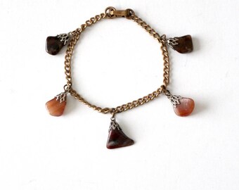 Pode incluir: Um bracelete de corrente dourada com cinco pingentes de pedra marrom e laranja. As pedras são engastadas em metal prateado.