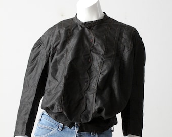 May include: A black, long-sleeved blouse with a ruffled collar and button closure. The blouse has a gathered, puffed sleeve and is made of a silky fabric.