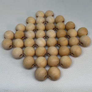 May include: A diamond-shaped trivet made from light-coloured wooden beads. The beads are connected by a thin wire. The trivet is designed to protect surfaces from hot items. The wood has a natural, warm tone.