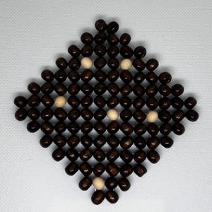 May include: A diamond-shaped trivet made of dark brown wooden beads, with a grid-like structure. The trivet has several light-colored beads interspersed throughout the design. This decorative item is suitable for protecting surfaces from hot dishes.