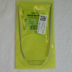 May include: A pair of 2.5 mm circular knitting needles, 60 cm long, made of aluminum. The needles are packaged in a clear plastic bag with a green and white label that includes the brand name "SKC" and other product information.