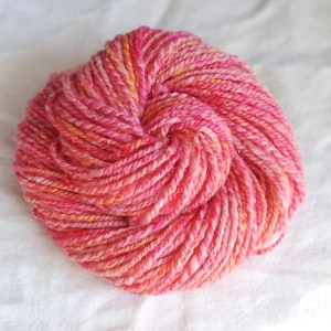 May include: A skein of pink and orange yarn with a sparkly finish. The yarn is twisted into a loose knot.