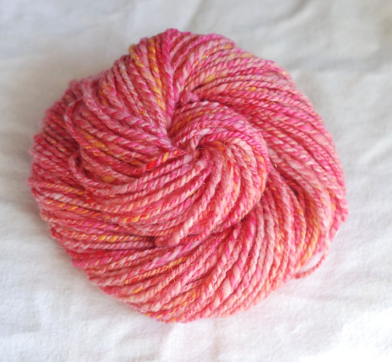 May include: A skein of pink and orange yarn with a sparkly finish. The yarn is twisted into a loose knot.