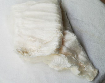 May include: A white fabric scarf with a soft, flowing texture. The scarf is folded in half and has a slightly wrinkled appearance.