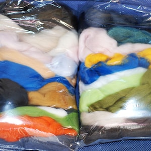 May include: Two clear plastic bags filled with various colours of wool roving. The bags are stacked on top of each other. The wool roving is arranged in layers of different colours, including white, pink, blue, yellow, green, and brown.