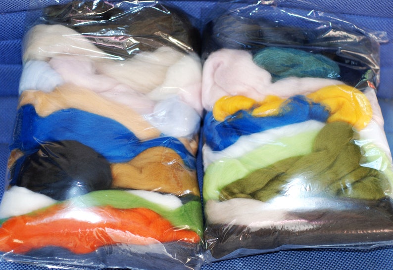 May include: Two clear plastic bags filled with various colours of wool roving. The bags are stacked on top of each other. The wool roving is arranged in layers of different colours, including white, pink, blue, yellow, green, and brown.