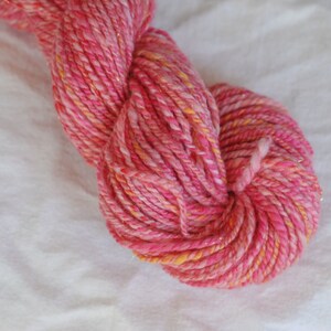 May include: Pink and orange yarn with a sparkly finish. The yarn is twisted and piled into a loose ball.