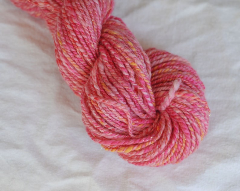 May include: Pink and orange yarn with a sparkly finish. The yarn is twisted and piled into a loose ball.