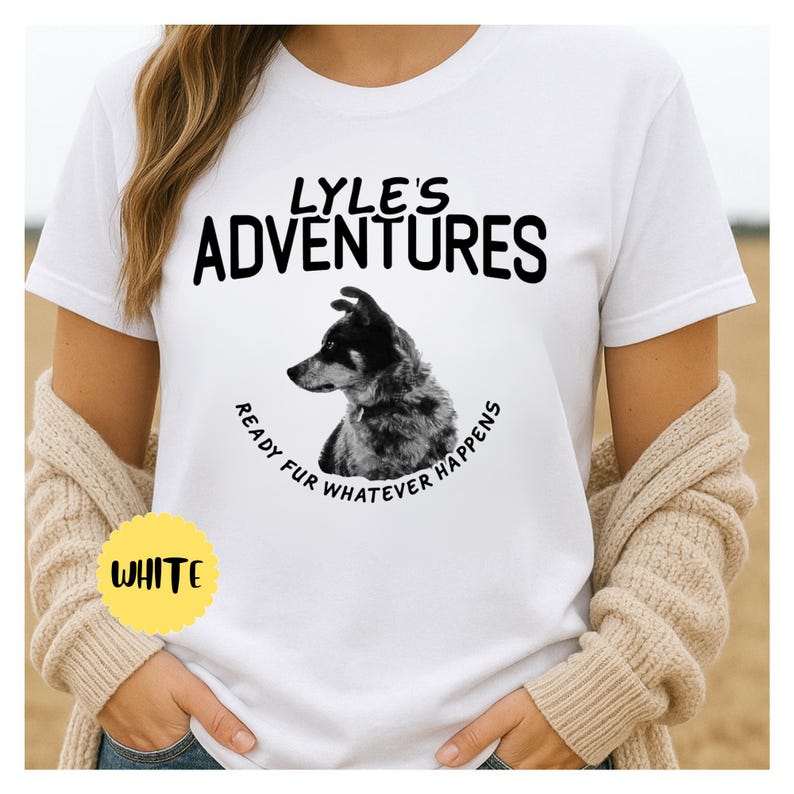 May include: White t-shirt with the text "LYLE'S ADVENTURES" above a black and white dog illustration. The phrase "READY FUR WHATEVER HAPPENS" is printed around the dog. A yellow circle with the word "WHITE" is in the lower left corner.