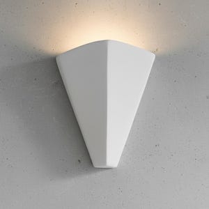 May include: A white, geometric wall sconce with a triangular shape. The sconce is mounted on a gray concrete wall, and a warm light shines from the top. The design is modern and minimalist.