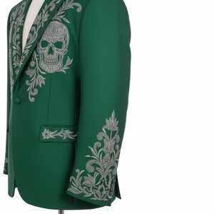 May include: A green blazer with detailed silver embroidery, including a skull motif on the chest and floral patterns. The jacket has a single-button closure and is tailored. The design is intricate and eye-catching, with a unique and detailed aesthetic.