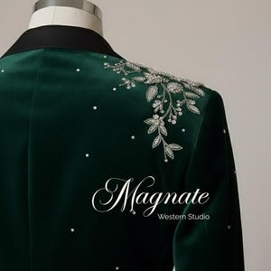 Puede incluir: Un blazer de terciopelo verde oscuro con cuello negro. El hombro est&aacute; adornado con bordados florales plateados y pedrer&iacute;a dispersa. La palabra "Magnate" y "Western Studio" est&aacute;n impresas en el blazer.