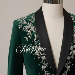 Puede incluir: Blazer verde esmeralda con solapas negras y bordados florales plateados. La chaqueta presenta el texto "Magnate Western Studio" en fuente cursiva.