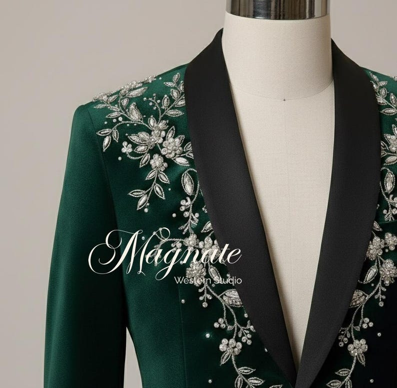 Puede incluir: Blazer verde esmeralda con solapas negras y bordados florales plateados. La chaqueta presenta el texto "Magnate Western Studio" en fuente cursiva.