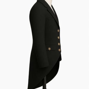 May include: A black tailcoat with gold-colored buttons, displayed on a mannequin. The formal jacket has a long, split tail and a classic, tailored design. The coat is made of a dark, possibly wool, fabric.