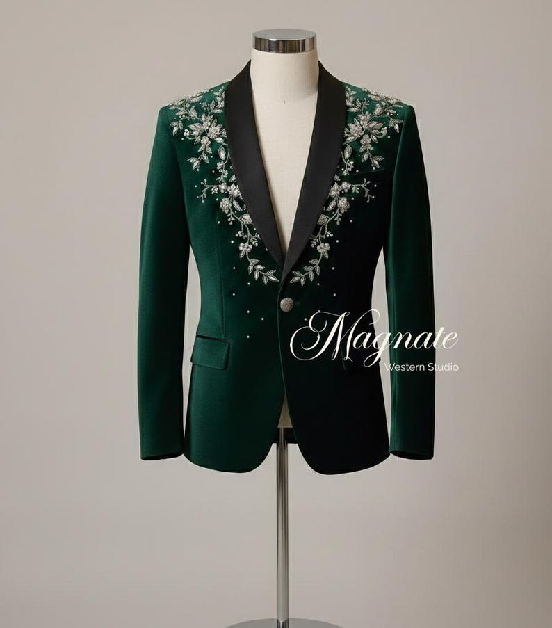Puede incluir: Una blazer de terciopelo verde oscuro con solapa de sat&eacute;n negro, adornada con bordados florales plateados y peque&ntilde;os detalles de cristal. La chaqueta tiene un cierre de un solo bot&oacute;n y el texto "Magnate Western Studio".