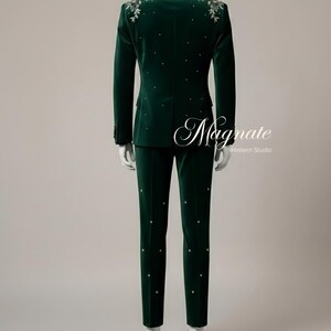 Puede incluir: Un traje de terciopelo verde oscuro con solapa negra, adornado con bordados florales plateados en los hombros y pedrer&iacute;a dispersa. El traje incluye una chaqueta y un pantal&oacute;n a juego. El texto "Magnate Western Studio" es visible.