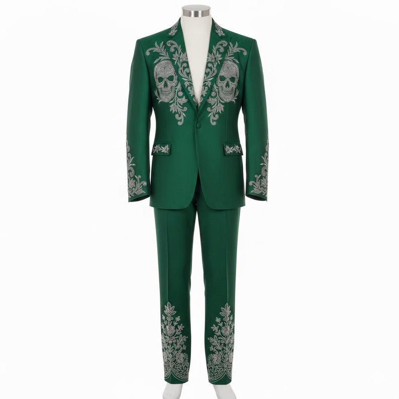 May include: A green suit with silver skull and floral embroidery. The jacket features two skull designs on the chest and floral patterns on the sleeves. The trousers have matching floral embroidery on the lower legs. The suit is displayed on a mannequin.