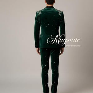 Puede incluir: Un traje de terciopelo verde oscuro con bordados florales en los hombros y adornos dispersos. El traje incluye una chaqueta y un pantal&oacute;n a juego. El texto "Magnate Western Studio" es visible en la imagen.