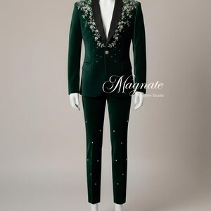 Puede incluir: Un traje de terciopelo verde oscuro sobre un maniqu&iacute;. La chaqueta tiene solapas negras y bordados florales en los hombros. Los pantalones tienen adornos decorativos. El texto "Magnate Western Studio" es visible.