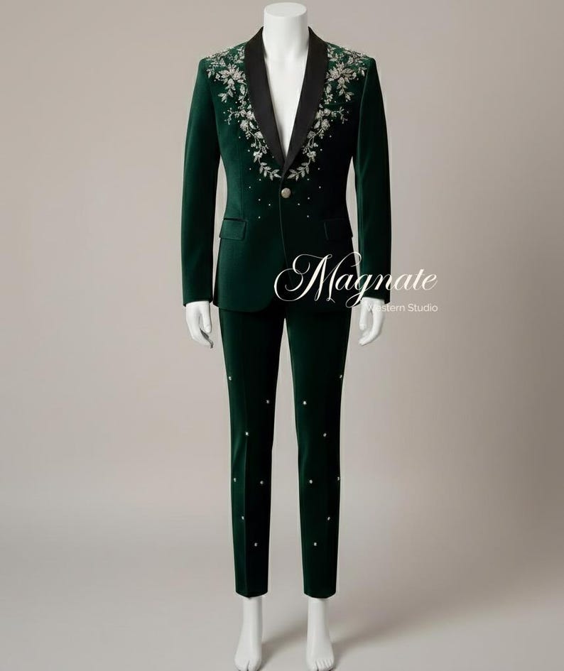 Puede incluir: Un traje de terciopelo verde oscuro sobre un maniqu&iacute;. La chaqueta tiene solapas negras y bordados florales en los hombros. Los pantalones tienen adornos decorativos. El texto "Magnate Western Studio" es visible.