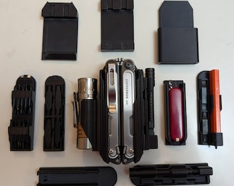 Può includere: Un utensile multifunzione Leatherman ARC con finitura argentata, posizionato centralmente tra vari componenti modulari in plastica nera, una torcia argentata, un coltellino svizzero rosso e un utensile arancione, disposti in piano.