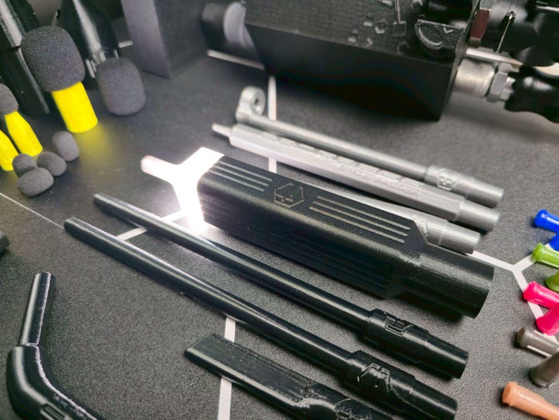 May include: A collection of 3D printed components including a black rectangular housing with a hexagonal logo, several long black and silver cylindrical rods, small black foam microphone covers, and various colorful plastic tips in a set.