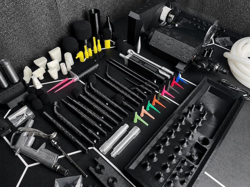 May include: A comprehensive set of black, white, and neon-colored automotive detailing tools, including various nozzles, brushes, a spray gun, a black storage tray with molded compartments, and a white hose, all arranged on a black surface.