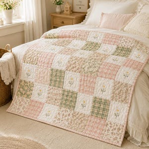 Könnte beinhalten: Eine Patchwork-Tagesdecke mit einem sich wiederholenden Raster aus Quadraten in zarten Pastelltönen wie Rosa, Salbeigrün und Weiß. Das Design wechselt zwischen einfarbigen weißen Quadraten mit gelben Blumenstickereien, rosa Karomustern und Blumenprints.