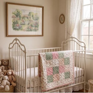 Könnte beinhalten: Ein weißes Metallgitterbett ist mit einer gesteppten Decke im Patchwork-Muster aus salbeigrünen und zartrosa Quadraten bedeckt. Das Bett steht in einem Raum mit einem gerahmten Landschaftsgemälde an der Wand und einem Korb voller Stofftiere.