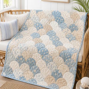 Könnte beinhalten: Eine gesteppte Tagesdecke mit einem sich wiederholenden Muschelmuster in den Farben Hellblau, Creme und Beige. Die Stoffbahnen zeigen verschiedene Blumen- und Sternenmuster, wobei sichtbare Nähte jede einzelne Muschelform nachzeichnen.