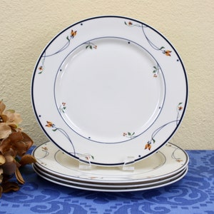 May include: Set of four white dinner plates with a blue and orange floral design. The plates are stacked on top of each other.