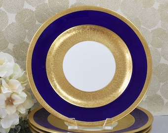May include: Set of four gold and blue rimmed dinner plates. The plates have a white center with a gold rim and a blue rim around the gold rim.