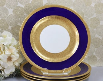 May include: Set of four gold and blue rimmed dinner plates. The plates have a white center with a gold pattern and a blue rim with a gold accent.