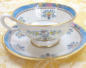 May include: A white teacup and saucer with a blue and gold rim. The cup and saucer are decorated with a floral pattern in shades of pink, yellow, and blue.
