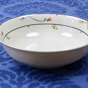 May include: A white ceramic bowl with a black rim and floral design. The bowl is on a blue patterned tablecloth.