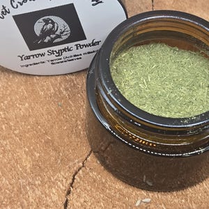Peut inclure: Un petit pot en verre ouvert rempli de poudre verte, à côté d'un pot avec un couvercle noir. Le couvercle porte une étiquette avec le texte "Velvet Crow Apothecary" et "Yarrow Styptic Powder". Les ingrédients sont répertoriés comme des fleurs et des feuilles de millefeuille.