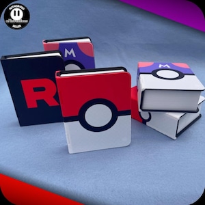 May include: A collection of small notebooks with various designs. One is red and white with a white circle, another is navy blue with a red "R", and others feature colourful designs. The notebooks are stacked on a light blue surface.
