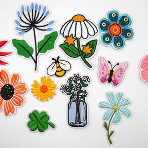 May include: A collection of colorful embroidered patches featuring various floral and nature-inspired designs. Includes a red starburst flower, orange sunflower, blue flower, bee, butterfly, and a mason jar with flowers. Perfect for adding to clothing or accessories.