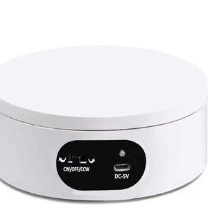 May include: A white circular rotating display stand with a flat top surface. The side features a black control panel with a three-position switch labeled CW/OFF/CCW, a small indicator light, and a micro-USB port labeled DC-5V for power input.