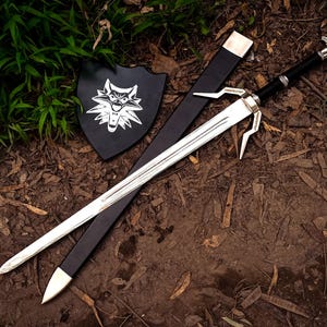 May include: A silver-toned steel sword with a black handle and a wolf-shaped pommel, accompanied by a black scabbard with silver metal accents and a black shield-shaped plaque featuring a white wolf head emblem printed on the surface.