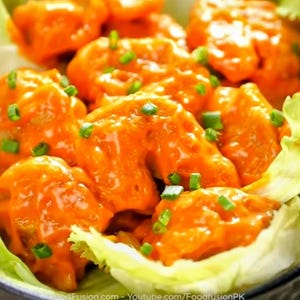 May include: A bowl of orange-glazed food, garnished with green herbs, sits on a bed of green lettuce. The food is likely an appetizer or snack. The image is a close-up shot.