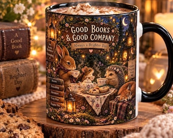 May include: A ceramic mug with a black handle and rim, featuring a detailed illustration of a rabbit, mouse, and hedgehog having tea in a forest. The text reads Good Books & Good Company, Always a Brighter Day, and lists words like Stories and Friendship.