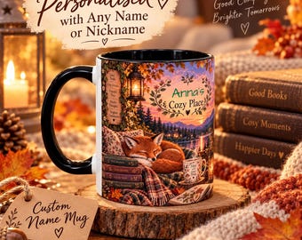 May include: A white ceramic mug with a black handle and rim, featuring a printed illustration of a sleeping fox on a stack of books, a lantern, and a sunset landscape. The text reads Anna's Cozy Place and Filled with Good Things.