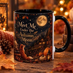 May include: A black ceramic mug featuring a printed autumn scene with a fox, pumpkins, a lantern, and a full moon. The text "Meet Me Under the Autumn Moon" is written in a decorative script font. The mug has a black handle and interior.