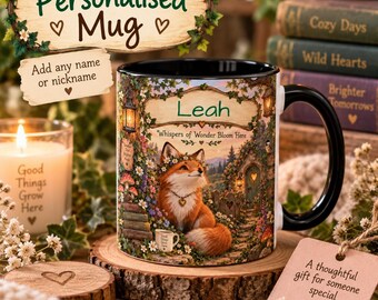 May include: A ceramic mug with a black handle and interior, featuring a printed illustration of a fox wearing a flower crown in a garden setting. The text on the mug reads Leah and Whispers of Wonder Bloom Here, with a small cup graphic.